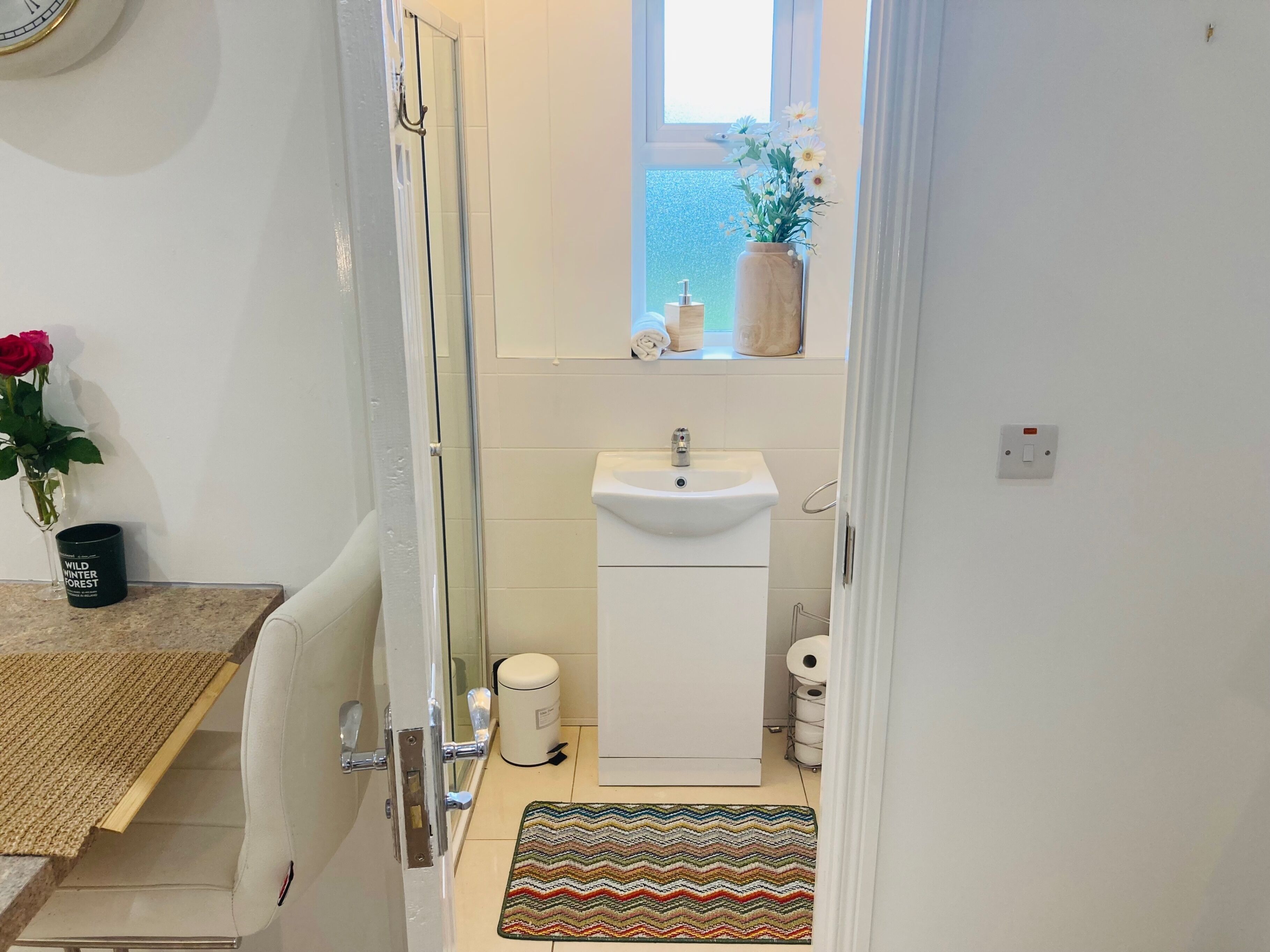 A compact bathroom with a sink, toilet, and shower. A window with a view of the sea is above the sink.