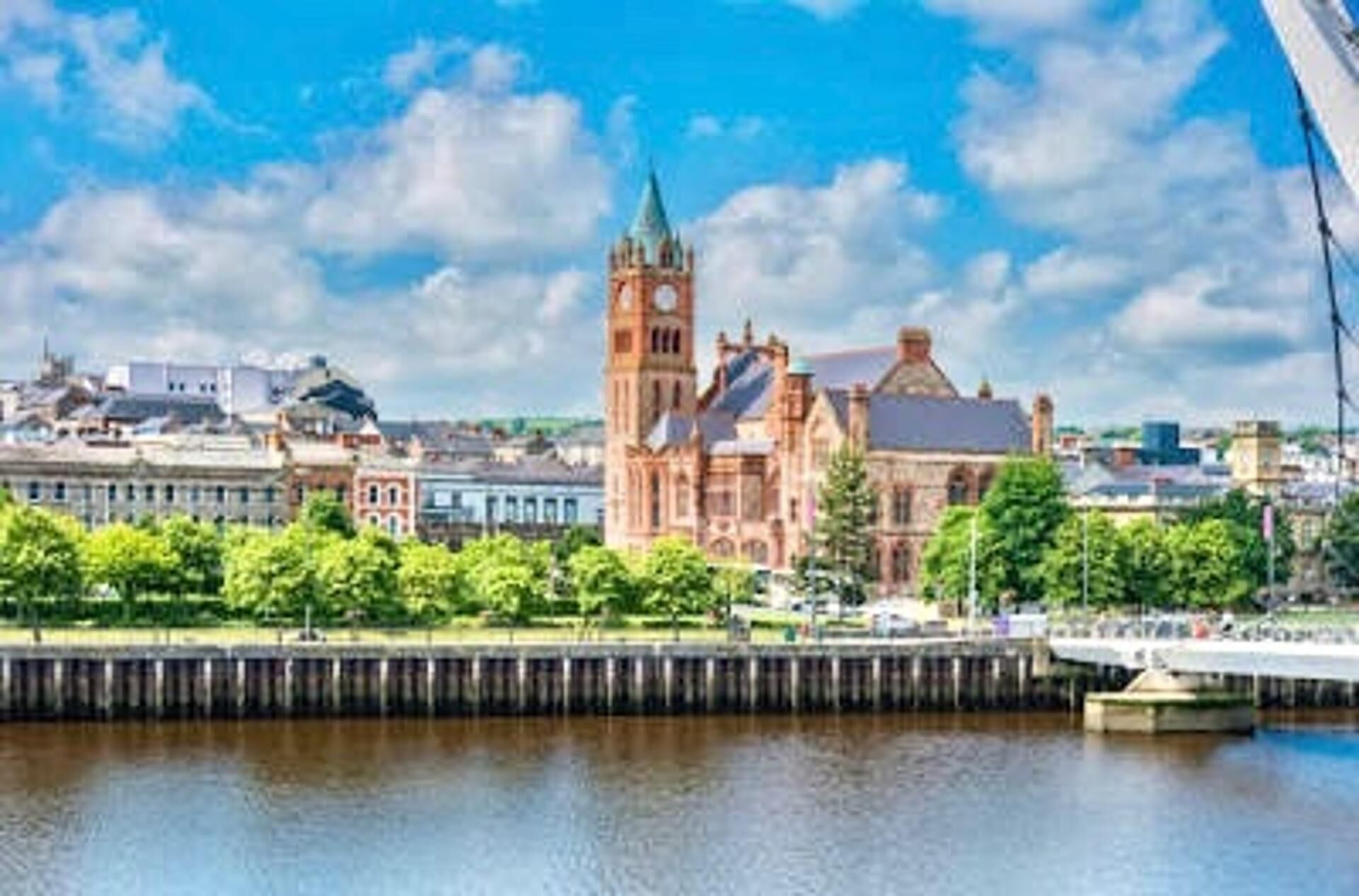 A historic building with a clock tower, a waterfront, and a bridge in the background.