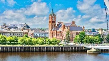 A historic building with a clock tower, a waterfront, and a bridge in the background.