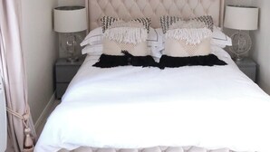 A neatly made bed with a tufted headboard, two bedside lamps, and a decorative throw pillow. - Cosy Studio Getaway - Free Parking & Central Links (South Ockendon)