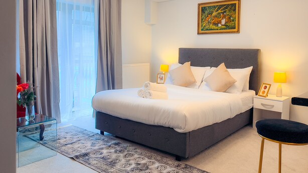 Un dormitorio moderno con una cama grande, lámparas de noche, un cuadro en la pared y vistas al exterior a través de la ventana.