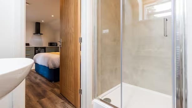 Een moderne badkamer met een douchecabine van glas, een houten deur en een zichtbaar wastafel.