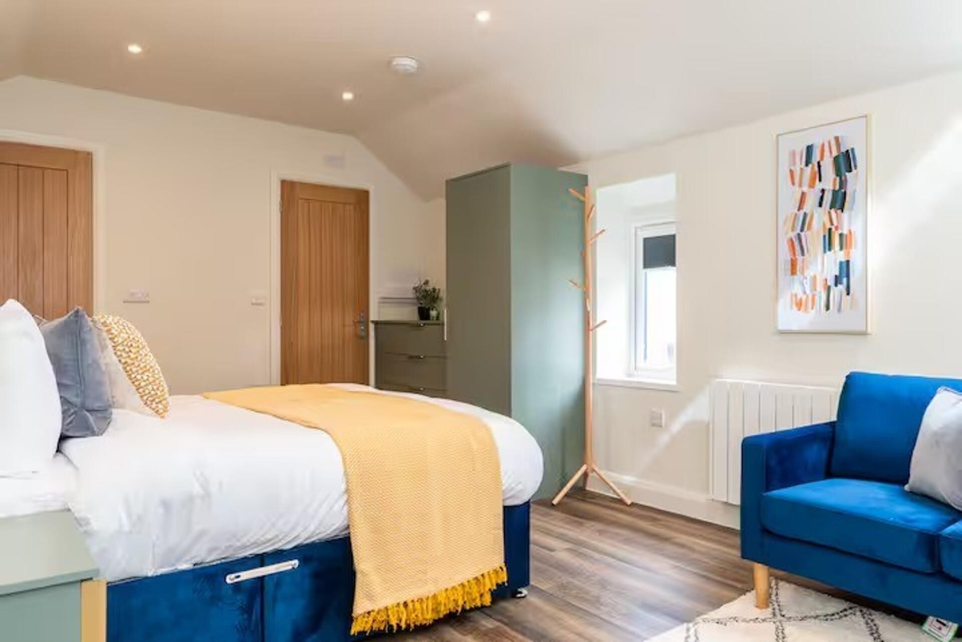 A bedroom with a bed, a blue chair, a wardrobe, and a radiator.