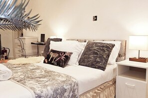 Ein ordentlich bezogenes Bett mit einem gemusterten Überwurf, zwei Zierkissen, einem Nachttisch mit Lampe und einer kleinen Kommode.