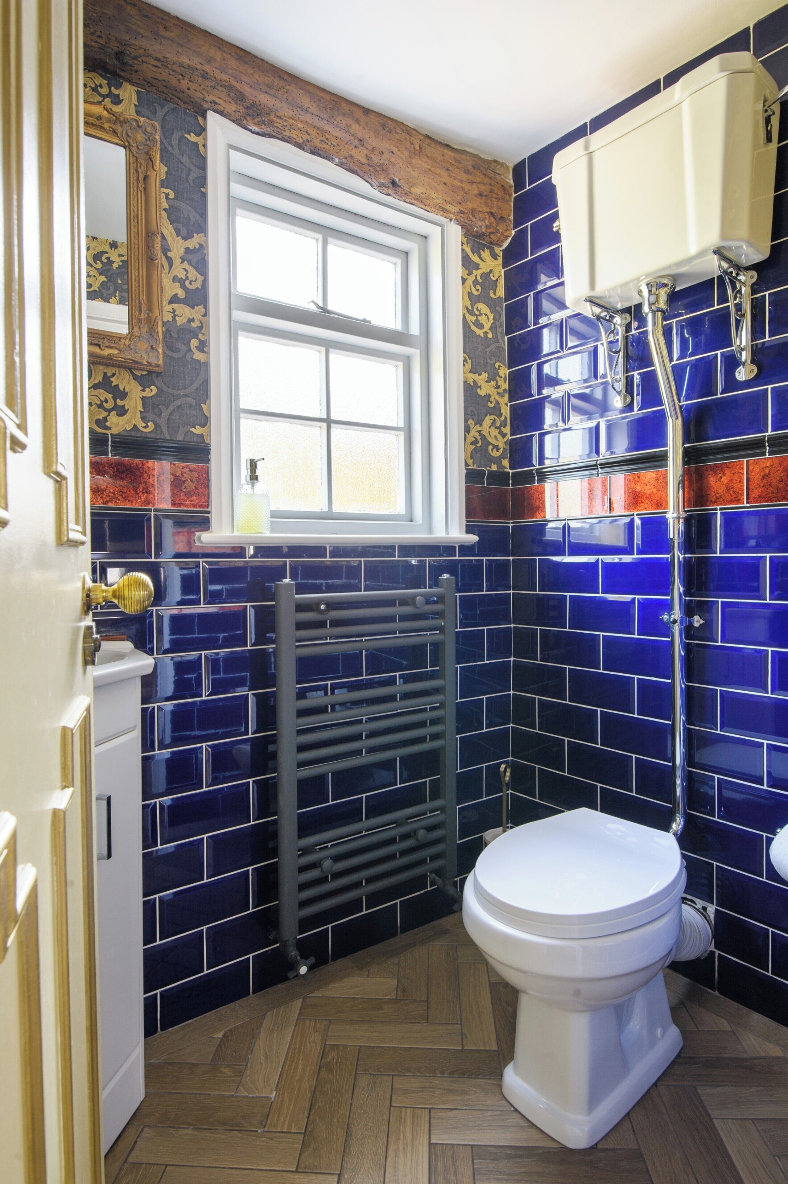 Un bagno con un water bianco, una finestra sopra e pareti rivestite di piastrelle blu.
