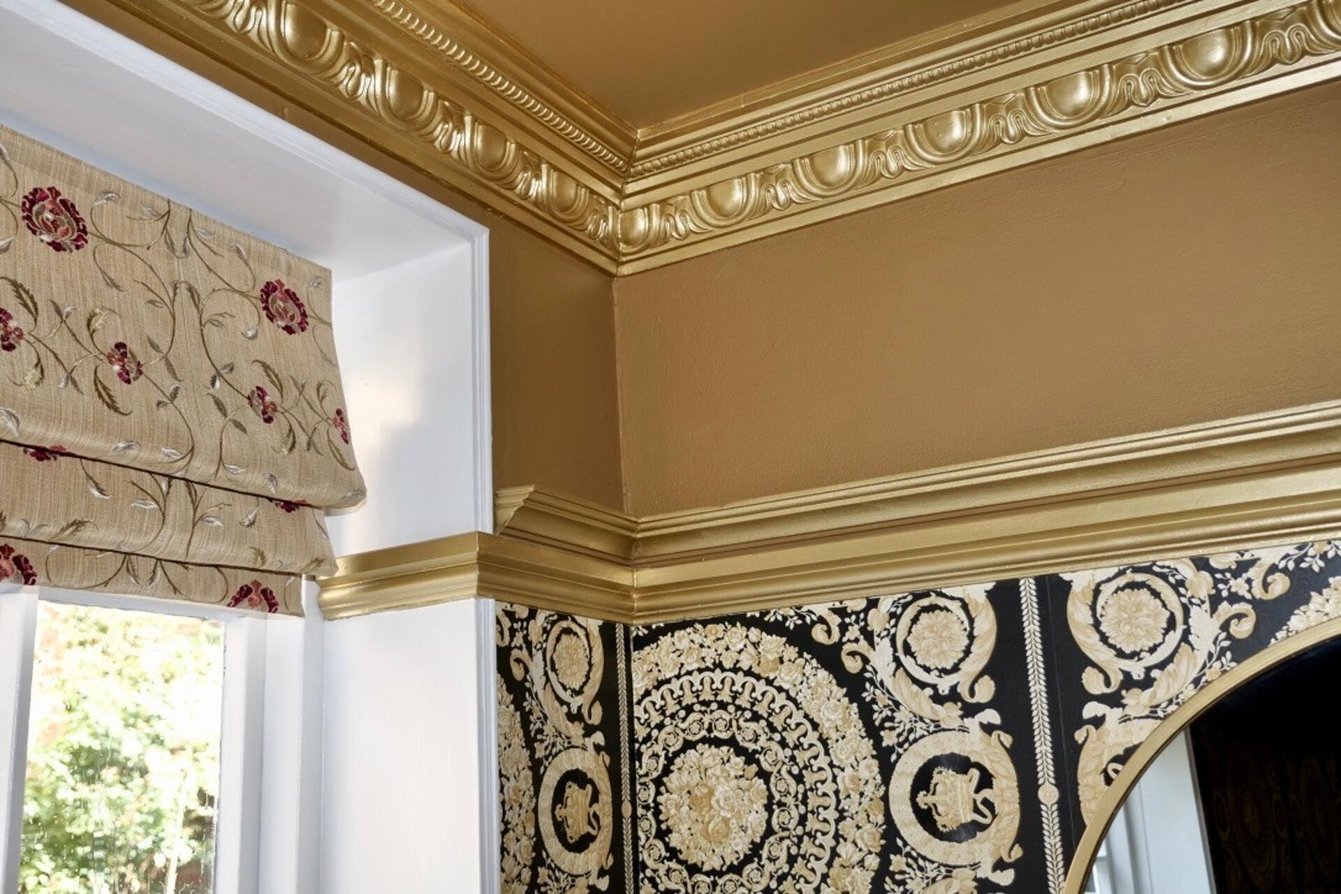 Una habitación con pared estampada, techo decorativo y ventana con cortina floral.