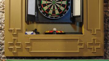A dartboard mounted on a wall with a green pool table below.