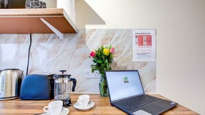 A wooden table with a laptop, two white cups, a teapot, a coffee maker, and a vase with flowers. - Bright Cosy Studio & Free Parking-greater London (Enfield)