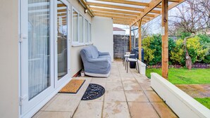 A covered patio with a sliding glass door, a cushioned seating area, and a small table. - Bright Cosy Studio & Free Parking-greater London (Enfield)