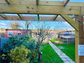 Eine Hollaube mit einem Garten darunter, einem Weg und einem roten Gebäude im Hintergrund.