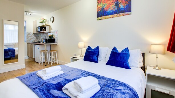 A hotel room with a bed, a desk, a chair, a mirror, and a painting on the wall. - Bright Cosy Studio & Free Parking-greater London (Enfield)