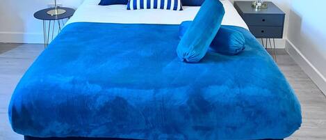 A bed with a blue cover, a striped pillow, and a matching pillow on a white mattress.