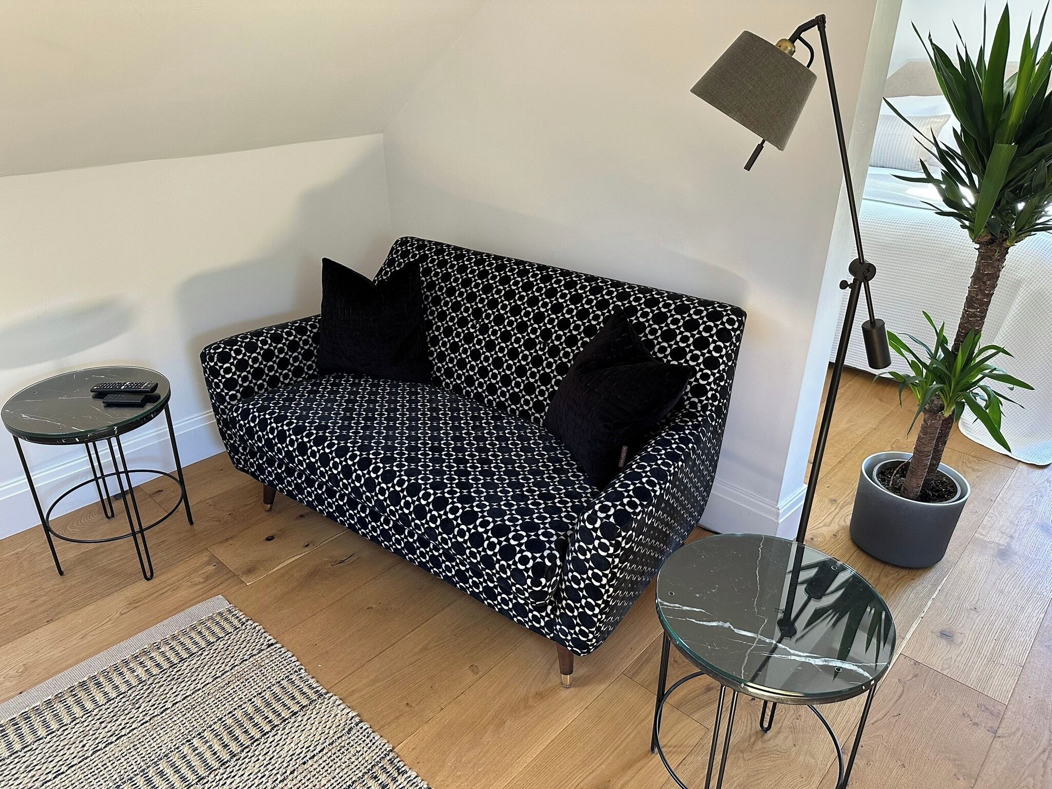 Una sala moderna con un sofá estampado, una mesita redonda, una lámpara de pie y una planta en maceta.