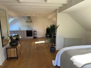 A modern loft bedroom with a sloped ceiling, wooden flooring, a large bed, a radiator, and a kitchen area with a stove and cabinets. - Hope Valley - Studio - Sleeps 2 - Parking (Hope Valley)