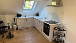 A compact kitchen with a skylight, white cabinets, a black stove, and a small dining area with a glass table and chairs. - Hope Valley - Studio - Sleeps 2 - Parking (Hope Valley)