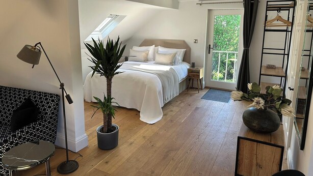 A bedroom with a bed, a potted plant, a bedside table, a nightstand, a hanging light, a wooden floor, a balcony door, and a view of greenery outside. - Hope Valley - Studio - Sleeps 2 - Parking (Hope Valley)
