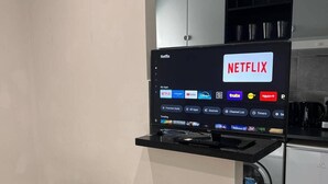 Televisão de tela plana presa a um suporte preto, exibindo o aplicativo Netflix e outros serviços de streaming.