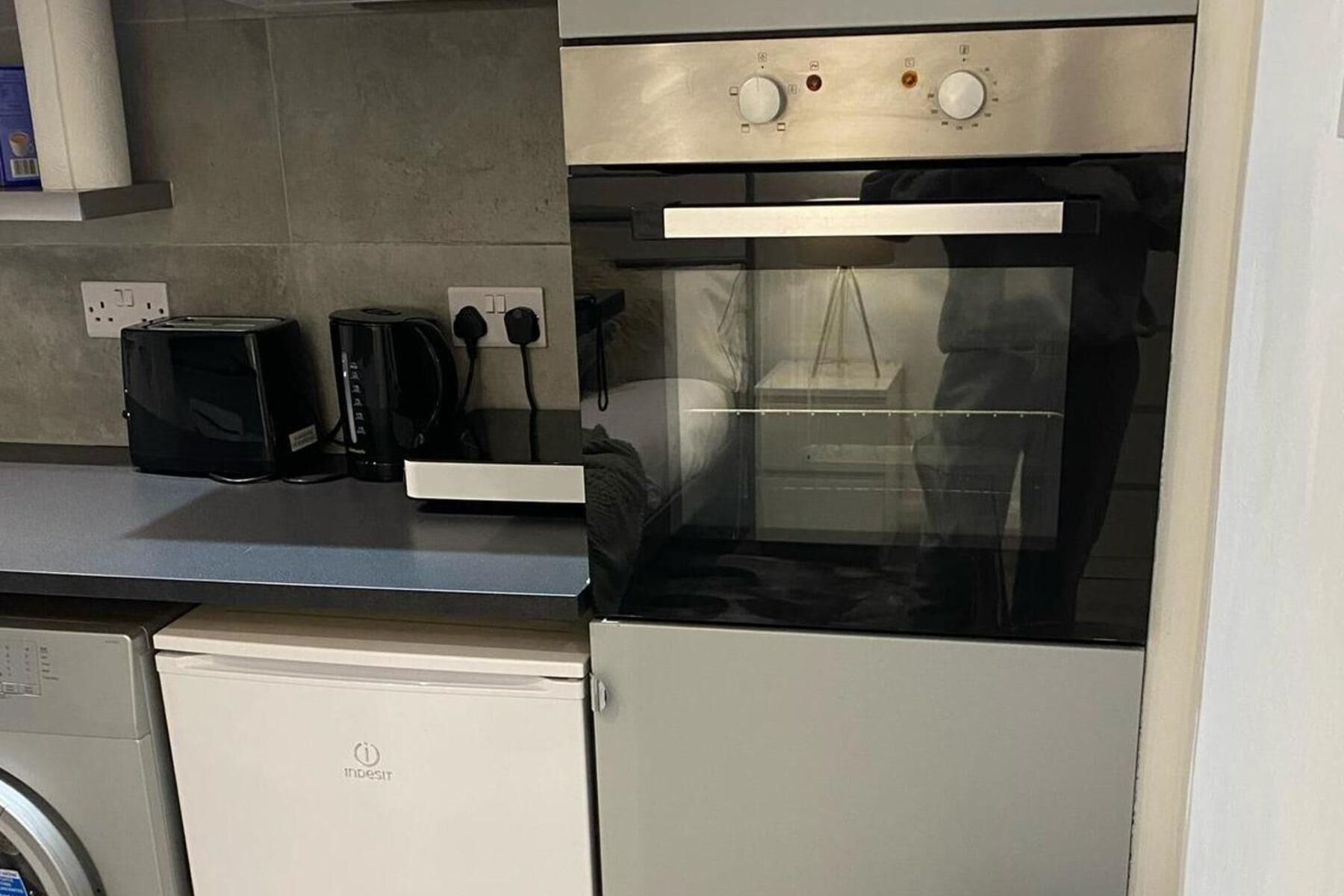 A compact kitchen with a built-in oven, a toaster, and a washing machine.