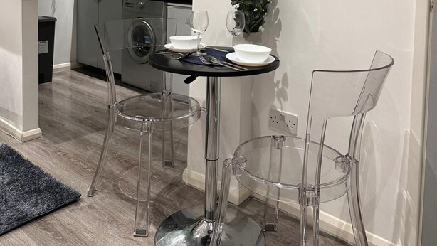Uma cozinha moderna com máquina de lavar, uma mesa de jantar com cadeiras transparentes e uma pequena planta em vaso.