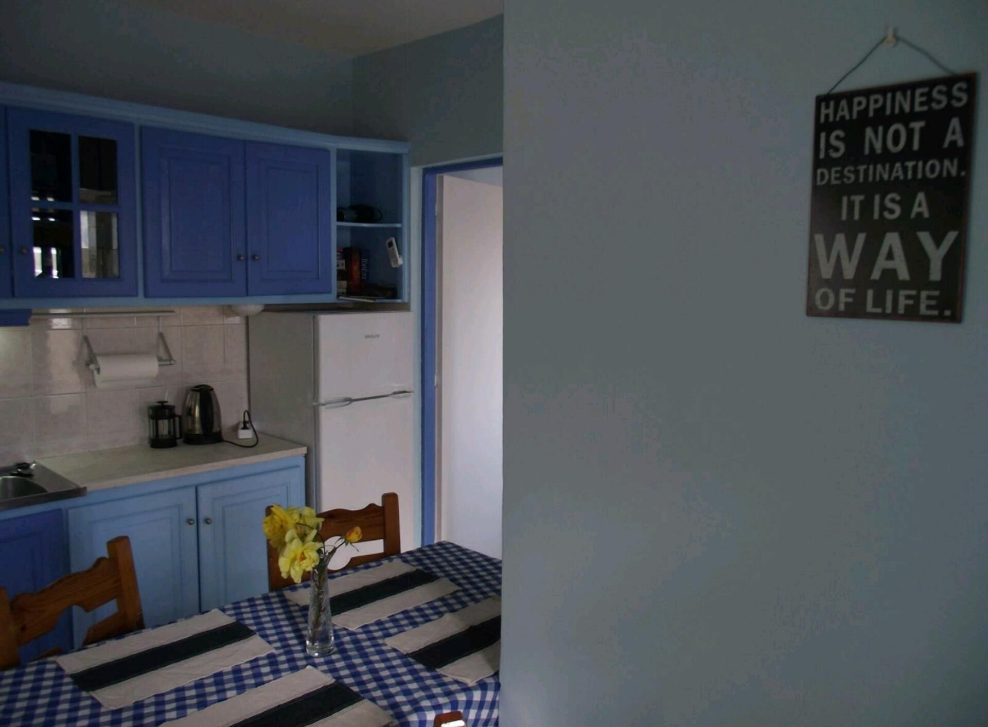 A kitchen with blue cabinets, a checkered tablecloth, and a vase with flowers.