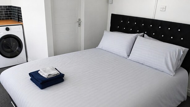 Un lit bien fait, avec du linge de lit blanc et deux oreillers, un lave-linge et une porte, dans une chambre d’hôtel.