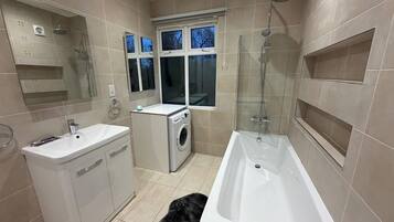 Un baño moderno con bañera, lavamanos, lavadora y ducha con mampara de cristal.
