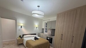 Quarto com cama, mesas de cabeceira, guarda-roupa, cozinha equipada com pia e fogão, e luminária pendente.