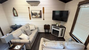 Una sala de estar acogedora con sofá, televisión, chimenea y una mesita de noche con lámpara.
