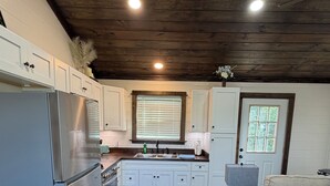 Una cocina moderna con armarios blancos, un refrigerador de acero inoxidable, techo de madera y una ventana con persianas.