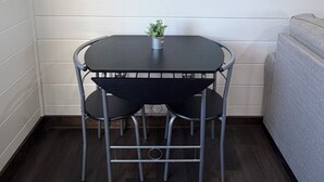 Un comedor con una mesa redonda, dos sillas, una planta en maceta y un adorno en la pared.