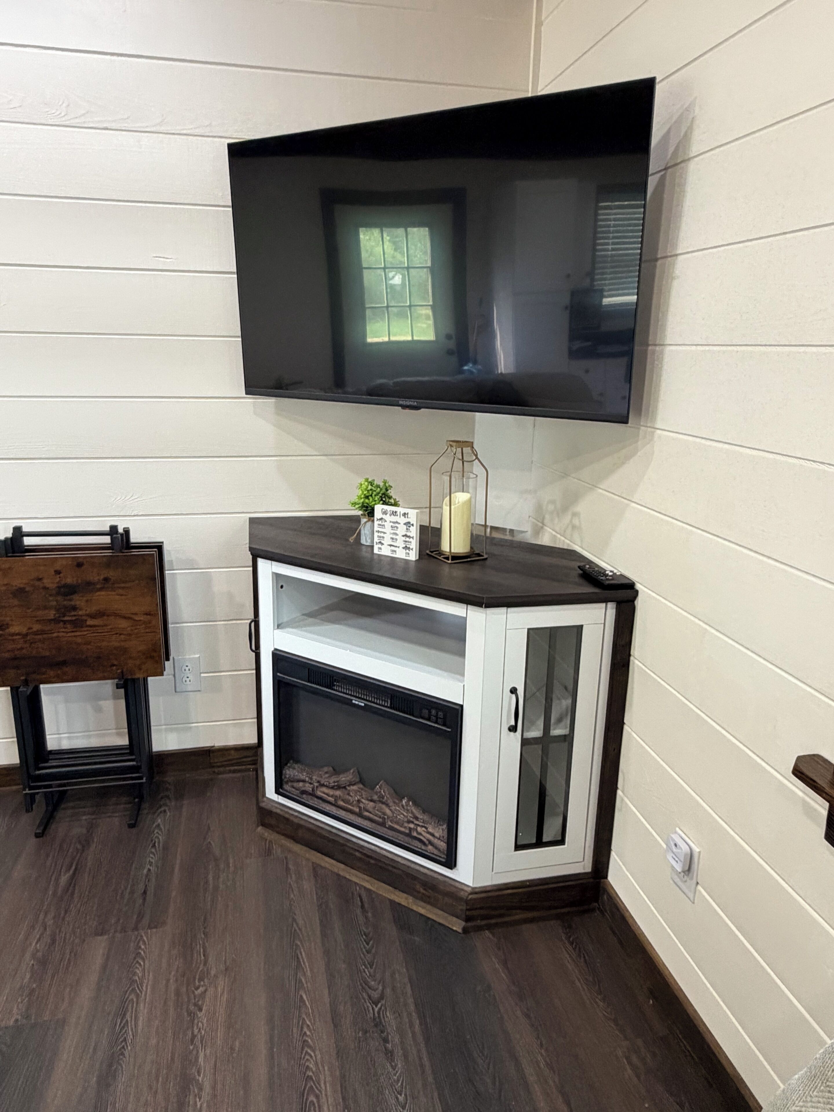 A living room with a mounted TV, a fireplace, a small table, and a bench.