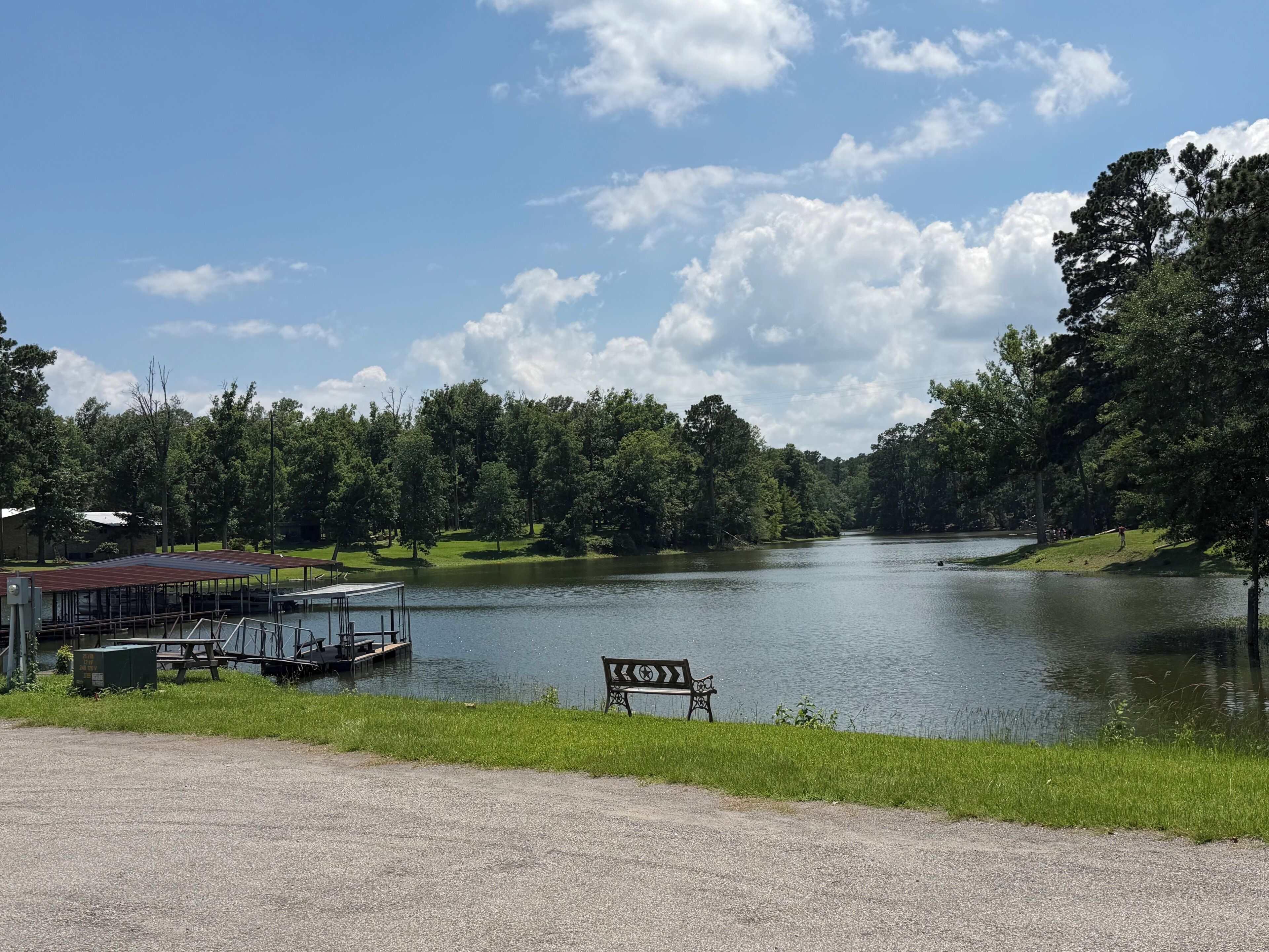 A lakeside view with a dock, a bench, and a building with a red roof.