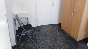 A room with a white door, a wooden wardrobe, a folding chair, and a carpeted floor. - Studio Sleeps 2 With Parking (Oldbury)