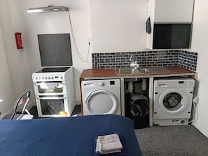 Ein kompaktes Hotelzimmer mit einem Bett, einer Küchenzeile, einer Waschmaschine und einem kleinen Waschbecken.