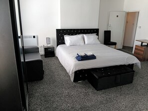 A hotel room with a bed, a nightstand, a desk, a wardrobe, and a small seating area. - Cozy Studio in Oldbury With Extra Beds (Oldbury)