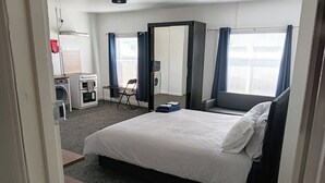 Ett hotellrum med en säng, ett skrivbord med en tvättmaskin, en stol och ett fönster med gardiner.