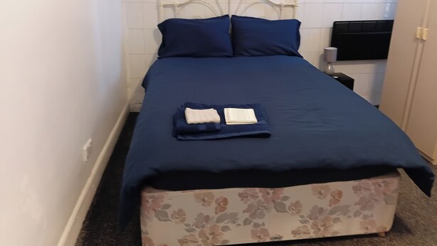 A single bed with a headboard, a blue bedspread, two pillows, and a small bedside table with a lamp. - Serene Studio Retreat in Oldbury (Oldbury)