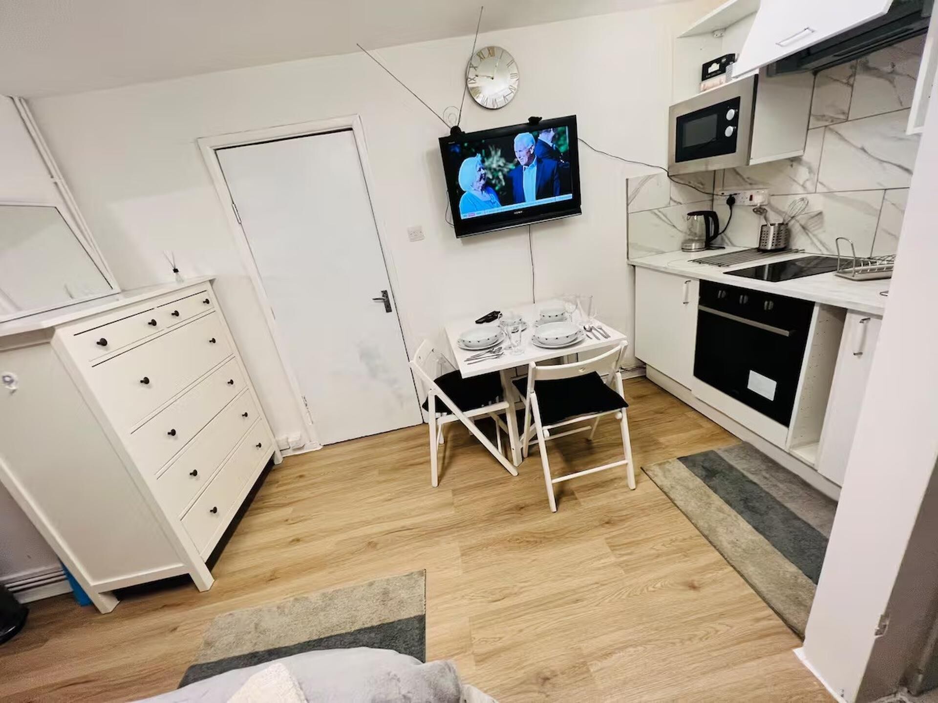 Uma cozinha compacta com uma mesa de jantar, uma TV na parede, micro-ondas e fogão.
