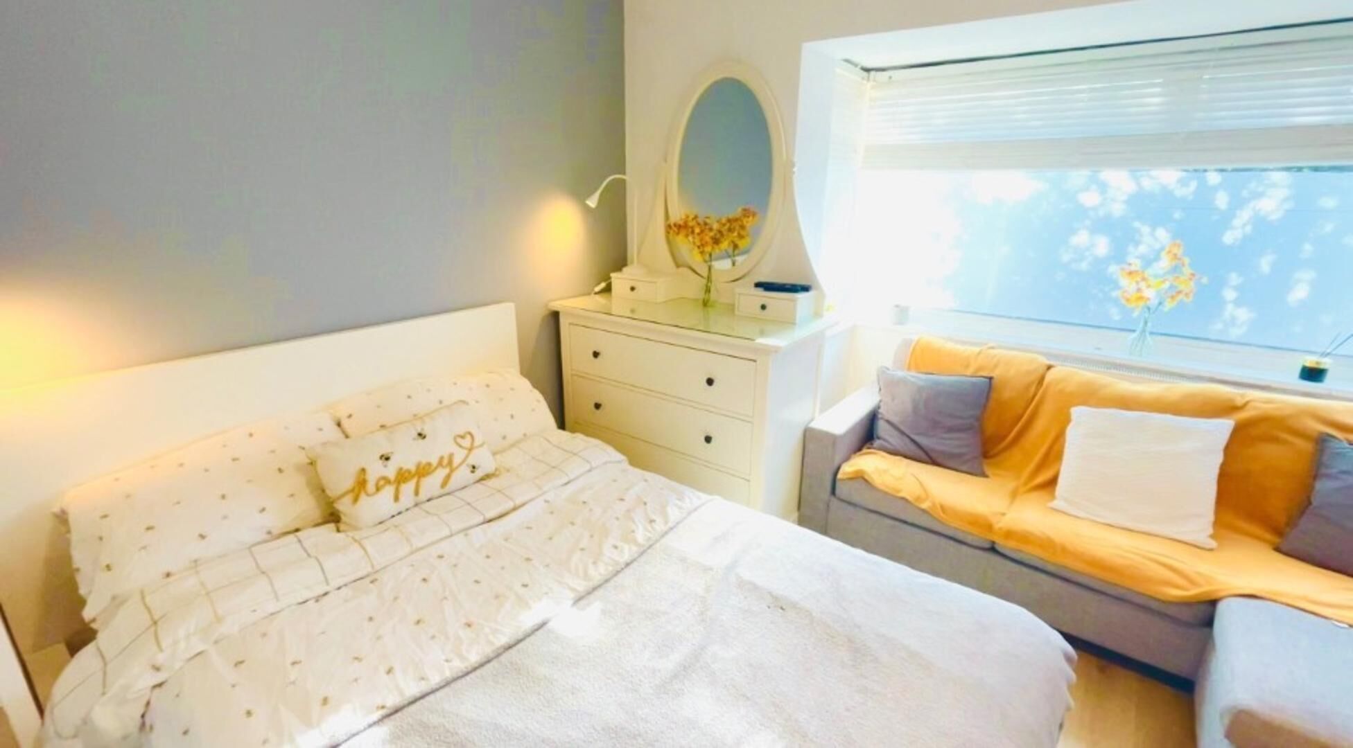 A bedroom with a bed, a bedside table with a mirror, a dresser, and a sofa.