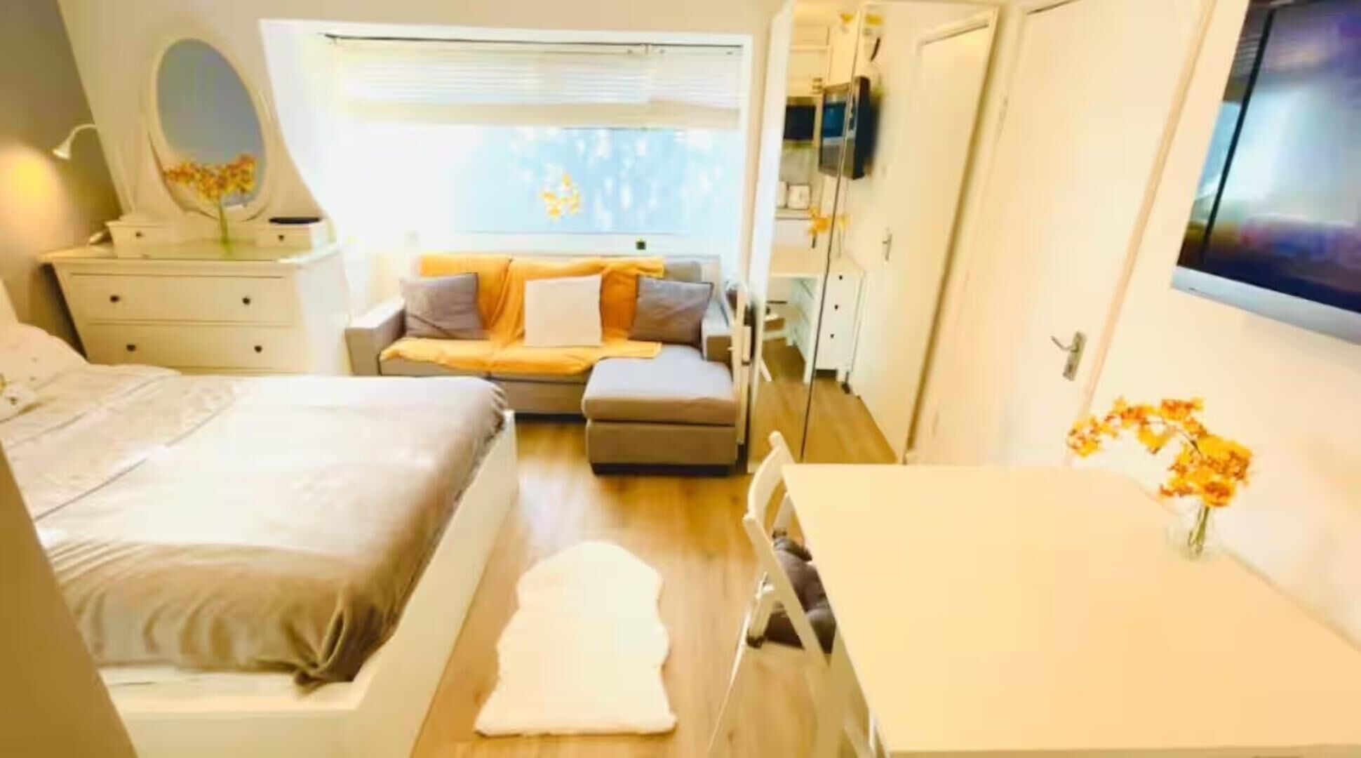 A bedroom with a bed, a desk, a chair, a sofa, a dresser, a mirror, and a window.
