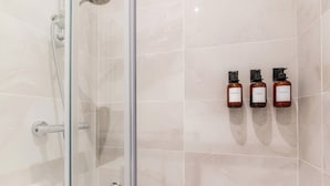 Eine begegnete Duschkabine mit Handbrause, drei Shampooflaschen an der Wand und ein gefliester Boden.