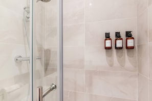 Eine begegnete Duschkabine mit Handbrause, drei Shampooflaschen an der Wand und ein gefliester Boden.