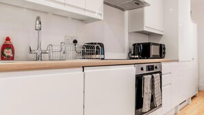 A modern kitchen with white cabinets, a stainless steel range hood, a microwave, and an oven.