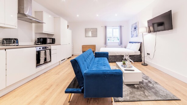 A modern apartment with a kitchenette, a blue sofa, a bed, and a TV.