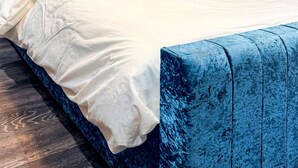 Une chambre à coucher moderne avec une tête de lit bleue, un couvre-lit blanc et un élément décoratif mural.