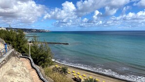 Vista costera con playa, océano y un pueblo lejano.
