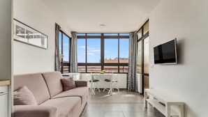 Una habitación moderna con sofá, mesa de comedor, sillas, televisor y ventanas amplias.