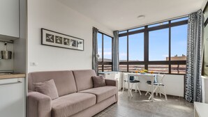 Una sala moderna con sofá, mesa de comedor y ventanas amplias.