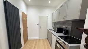 A narrow kitchen with a black radiator, white cabinets, a microwave, and a stove. - Studio - Sleeps 2 - Air Con - Parking (London)