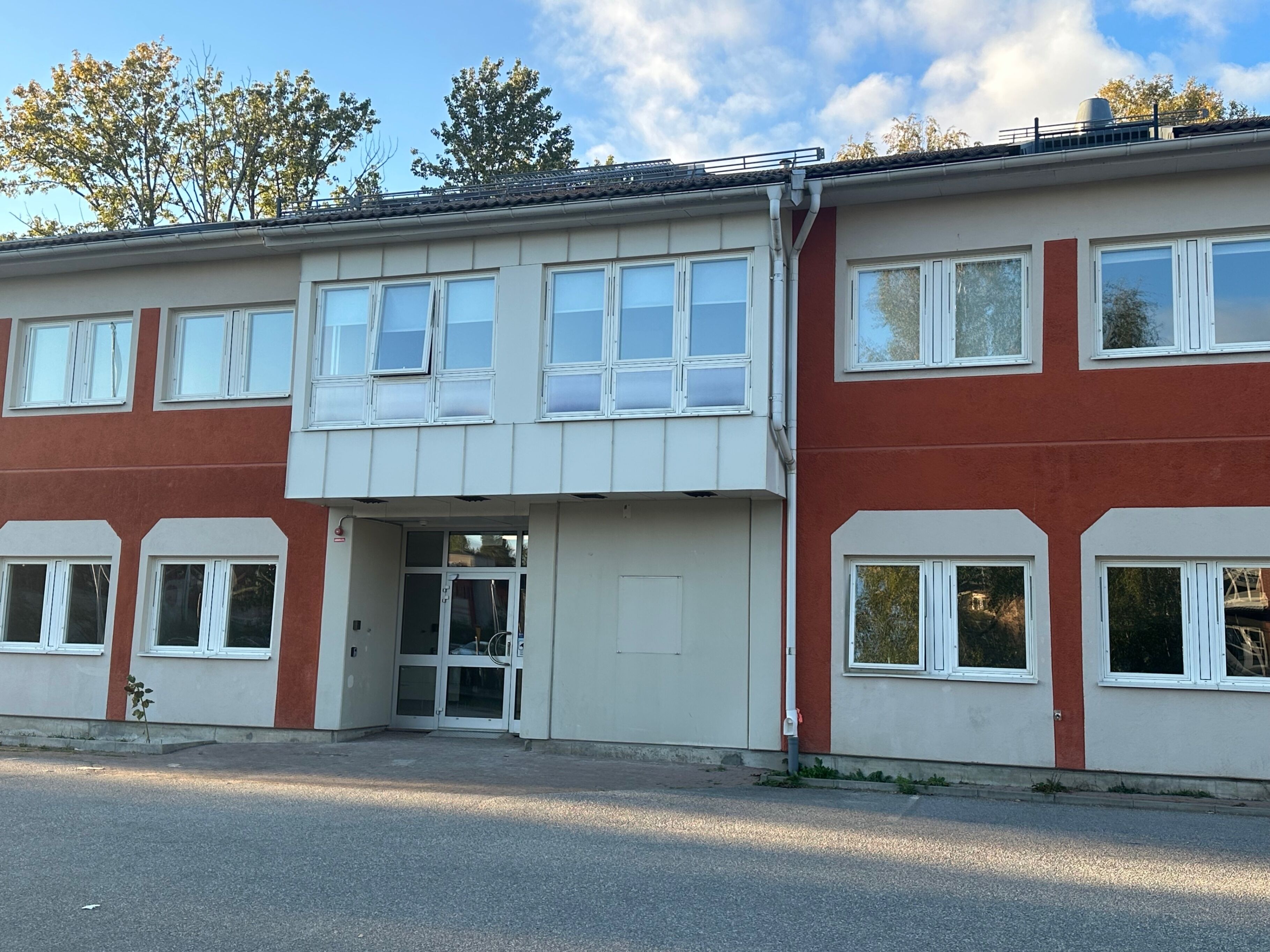 A two-story building with a flat roof, large windows, and a central entrance.